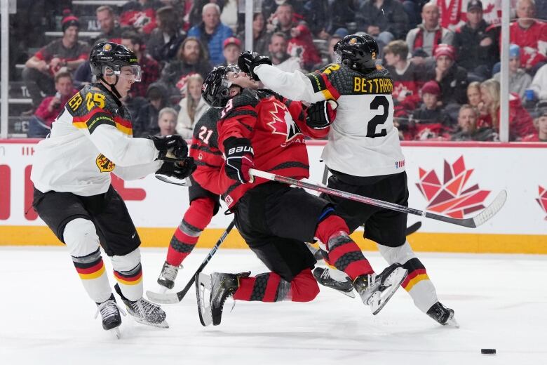 A Canadian hockey player is seen being hit in the face by a German player. The Canadian's face is titled back due to the contact and both his skates aren't in contact with the ice as he's in falling down.