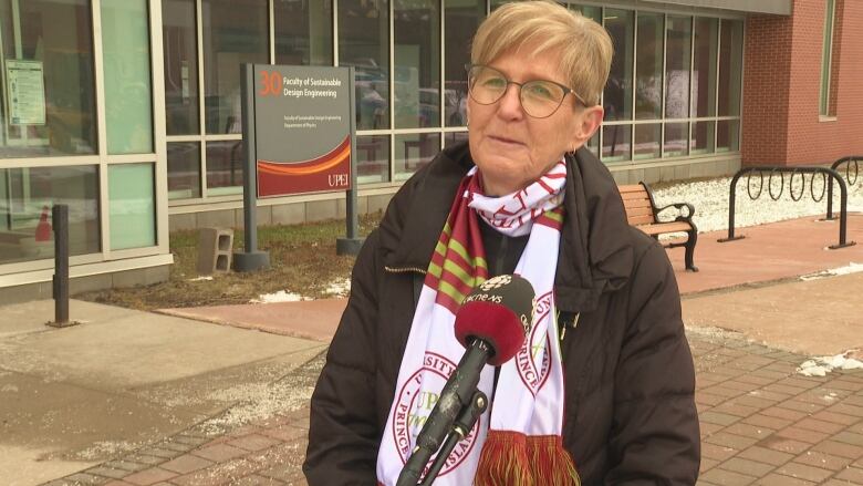 Woman stands in front of university building with UPEI alumni scarf on