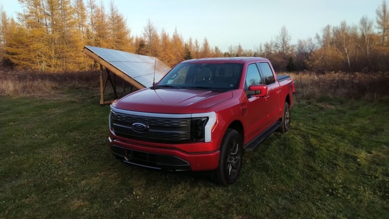 A red Ford truck parked next to an angled collection of solar panels. There are orange trees in the background.