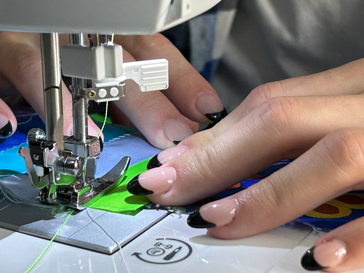 A close up of hands feeding ribbon through a sewing machine.