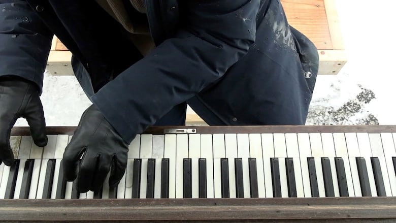 Looking down on a set of gloved hands hovering over piano keys.