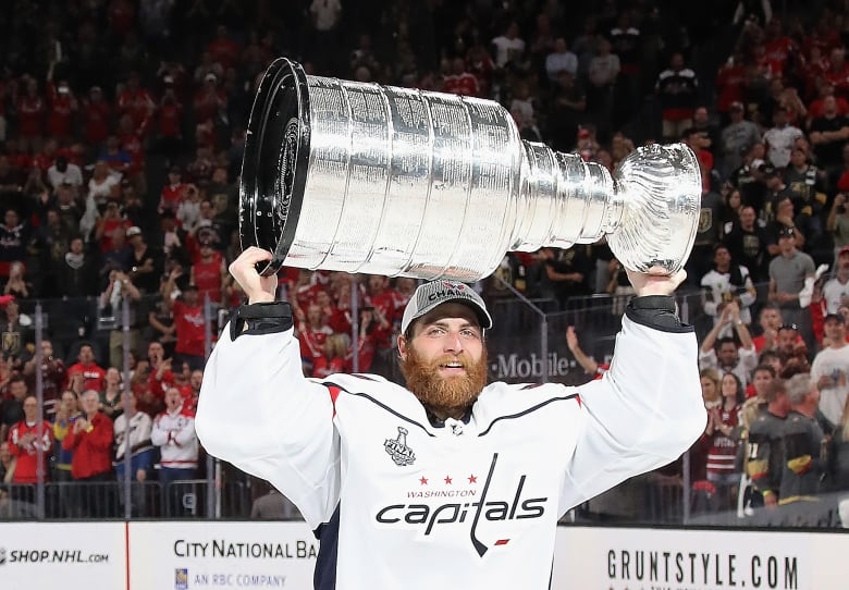 Hockey player holds Stanley Cup trophy over his head.