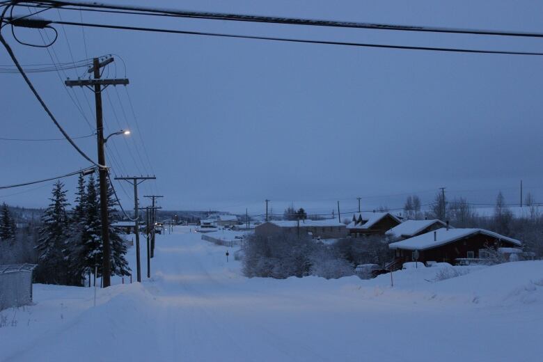 A photo taken from a road, with power lines on the left and looking down on snow-covered homes to the right and in the distance. It's dawn and there's isn't a lot of light - and street lights are on.