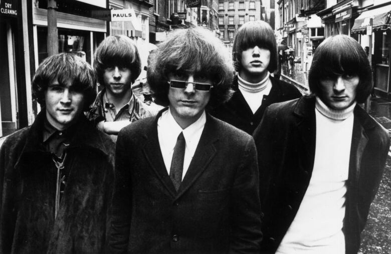 A black and white photo of five men walking down a street.