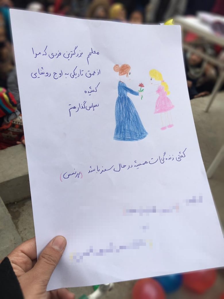 A hand holding a paper that features a drawing of a teacher sharing a flower with a student.