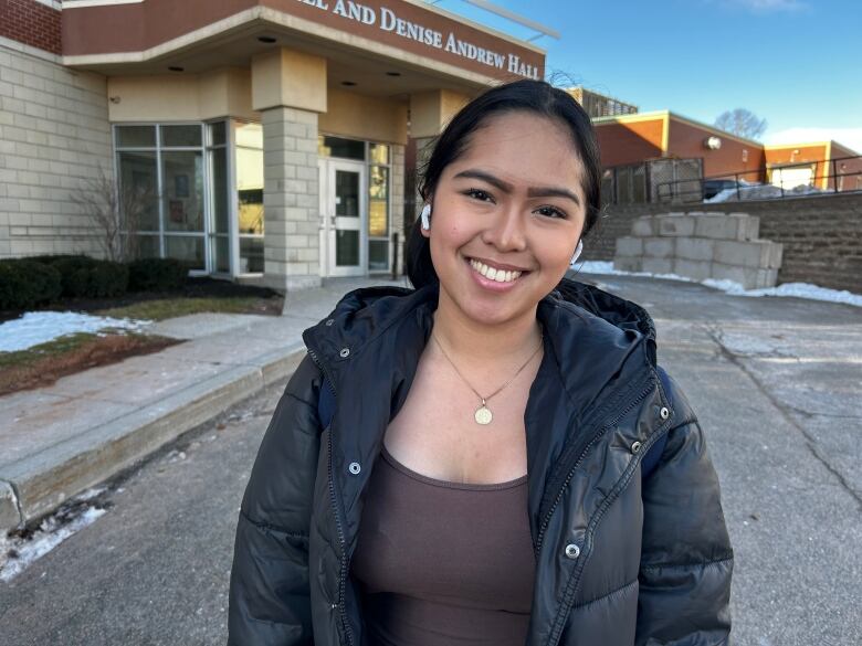 Portrait of a woman in a black down jacket standing in front of a residence hall. 