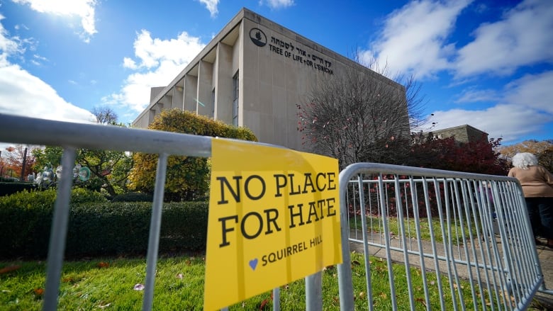 A yellow sign that reads "No Place For Hate" hangs on a fence outside a synagogue.