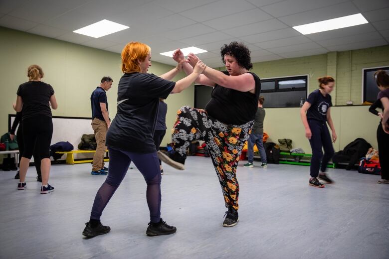 Two women practise martial arts moves in a classroom. 