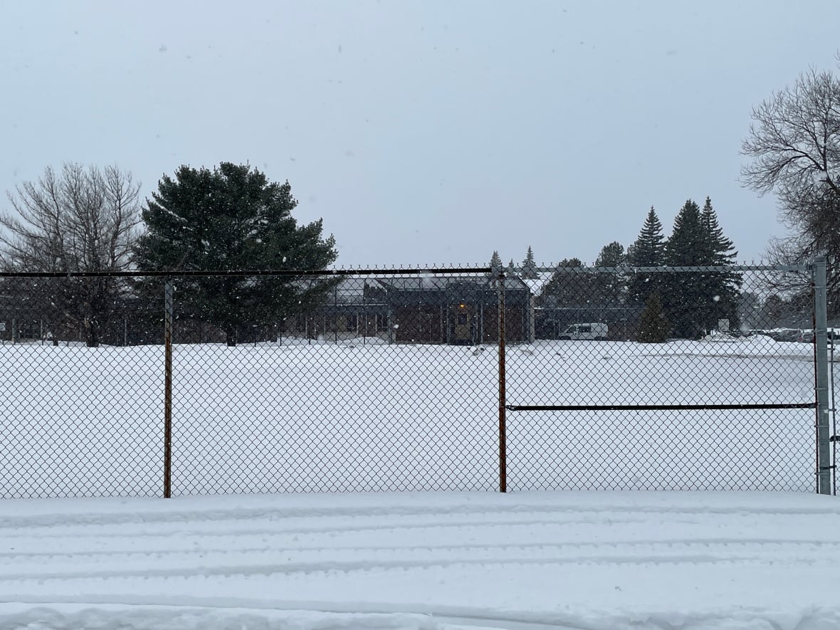 A chain-link fence with a large brown building behind it.