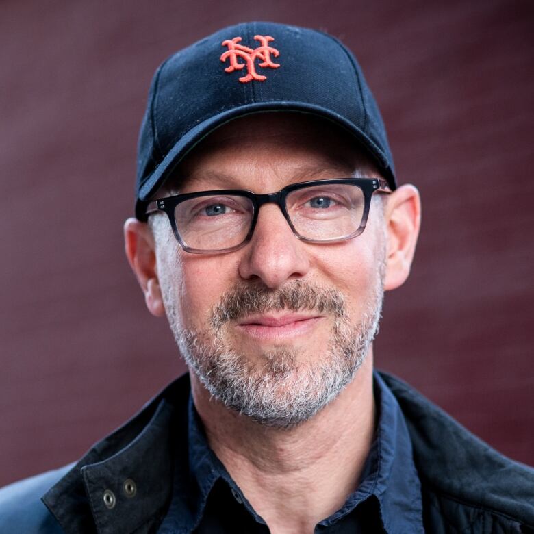 A portrait of a smiling man with a beard, glasses and baseball cap. 