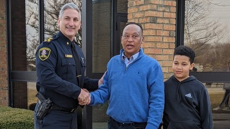 Police chief shakes hand of man, who is standing next to a boy.