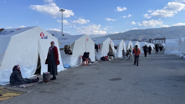 People stand outside a row of white tents.