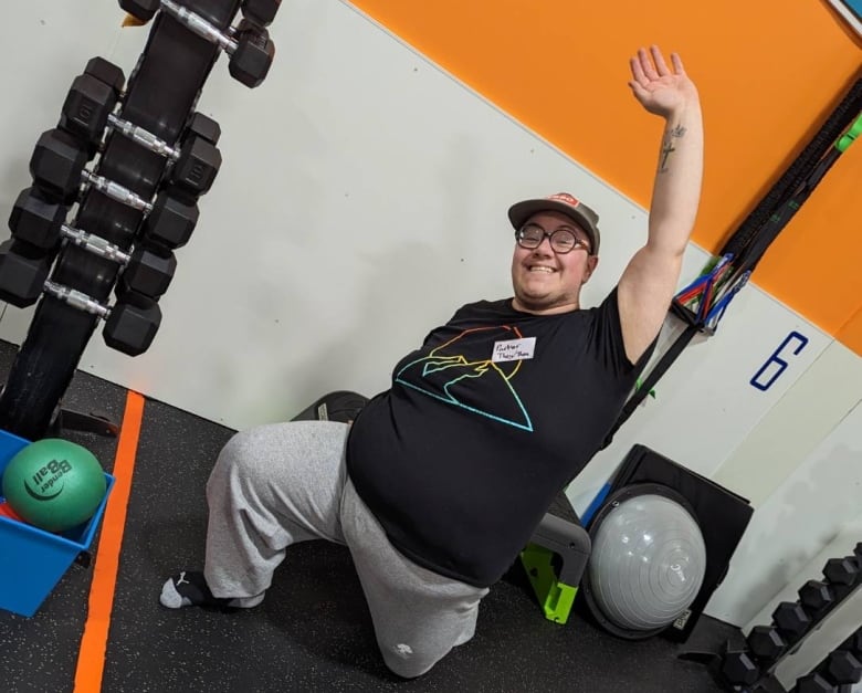 A person stretches on the floor of a gym next to weights, with one arm raised above them.