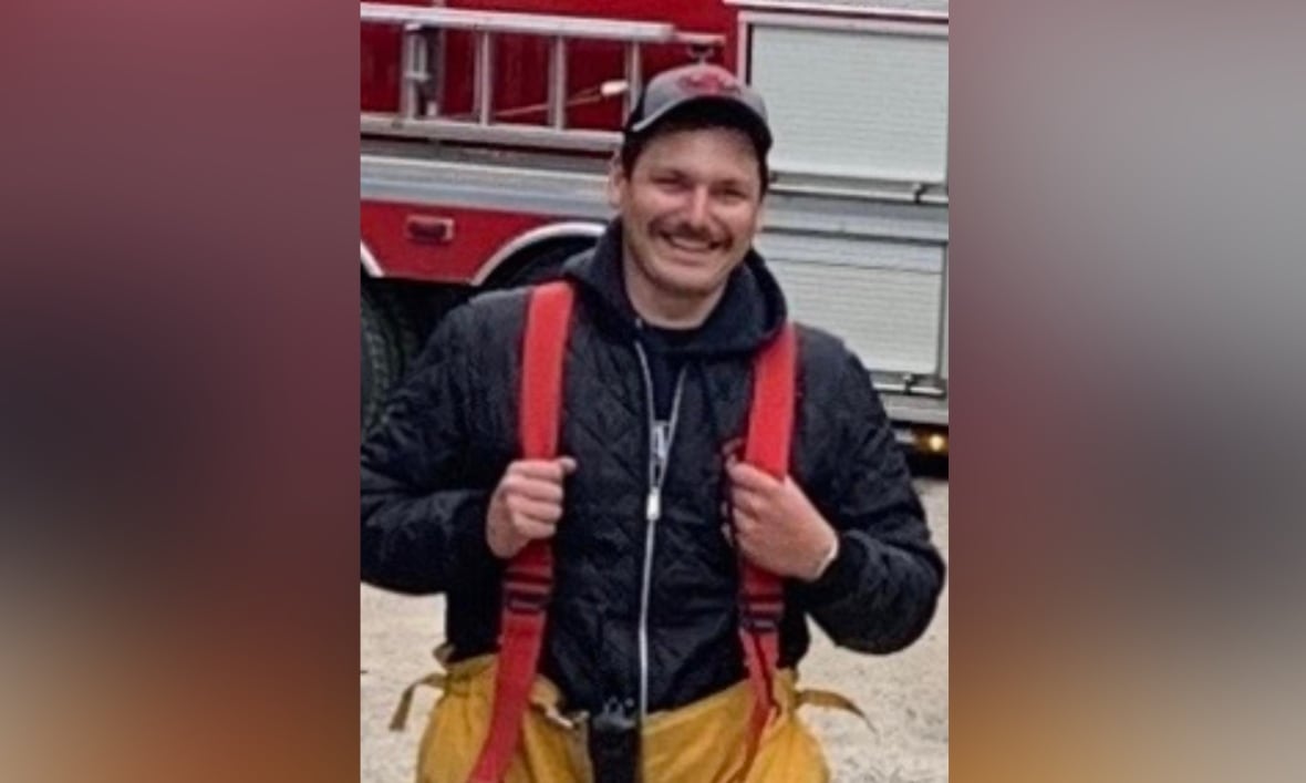 A man with red suspenders stands in front of a firetruck, smiling for a photo