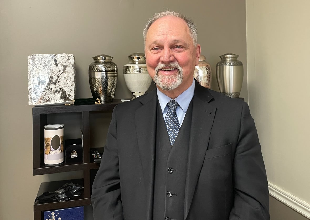 Collin Bourgeois stands in front of a shelf full of brass urns.