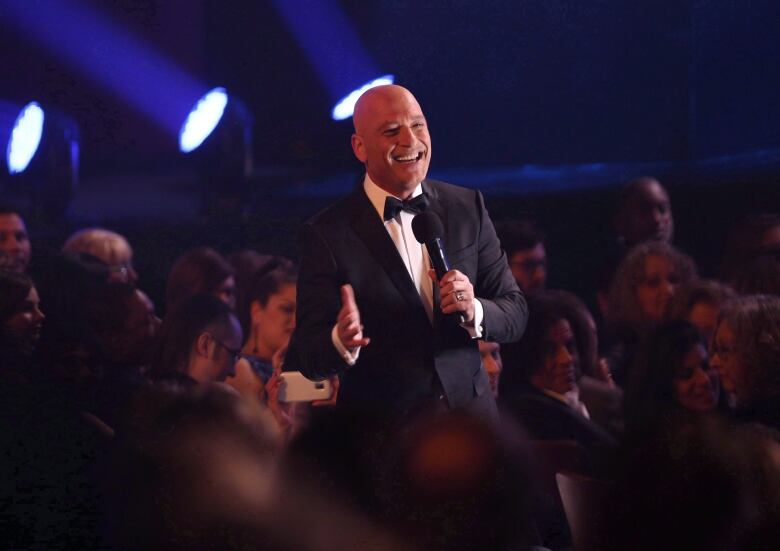 Howie Mandel is in the middle of an audience at a comedy show where everyone's laughing.