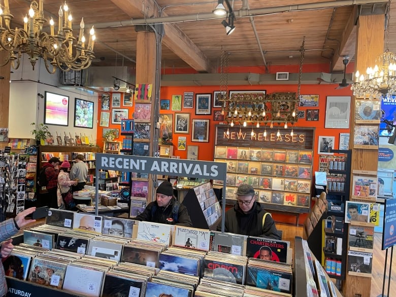 The inside of a record store. Some people browse titles. The sign says new releases.