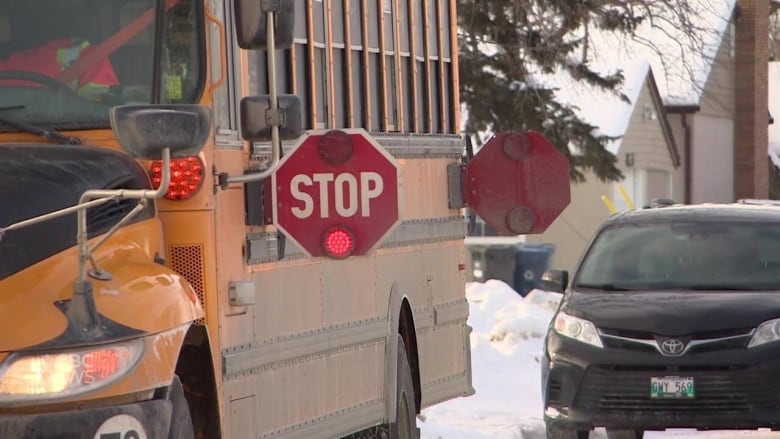 A closeup of the front of a yellow school bus parked on a snow-covered street with a red "stop" sign extended on its side.