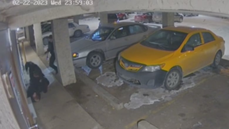 A police officer kneels on a man on the ground in a parkade, raising his arm as if to strike the man. A second police officer approaches the pair from behind. 