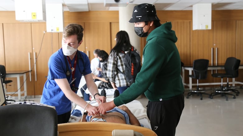 Young people wearing surgical masks working on a patient in a classroom setting.