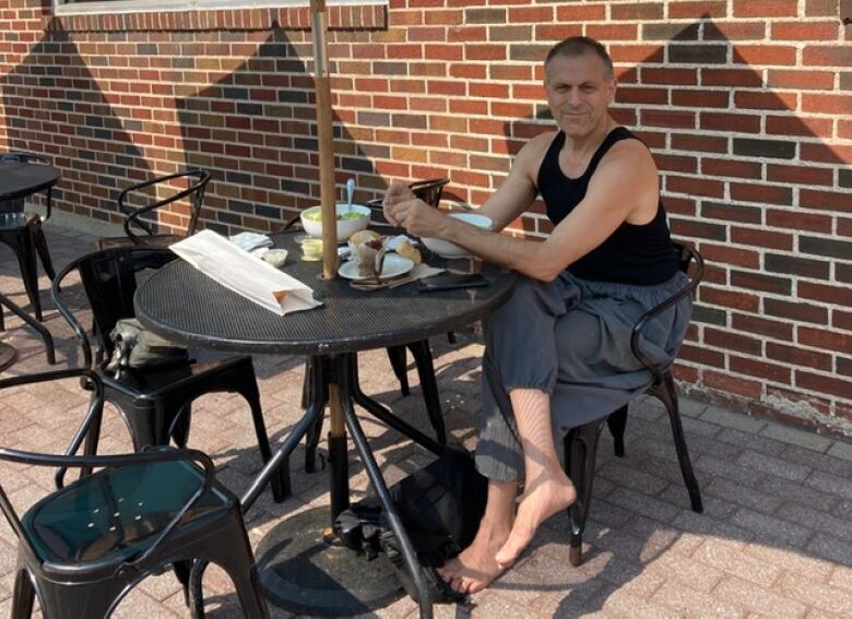 A barefoot man sits at a patio table at a restaurant.