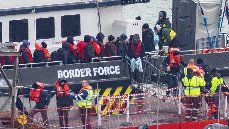 Several people, many in life vests, disembark a large boat.