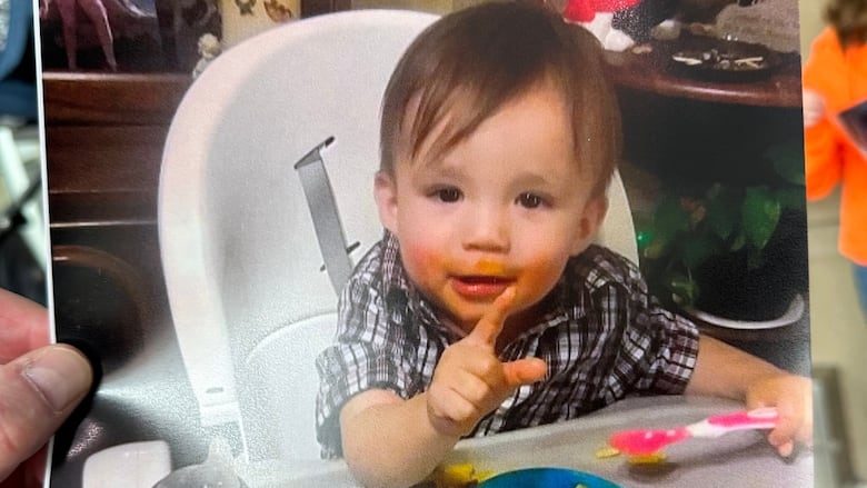 A toddler sits in a high chair eating a bowl of food.