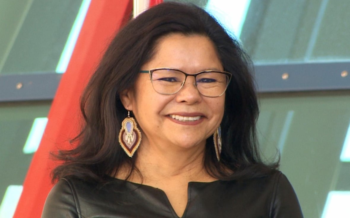 A dark-haired woman with glasses is smiling.
