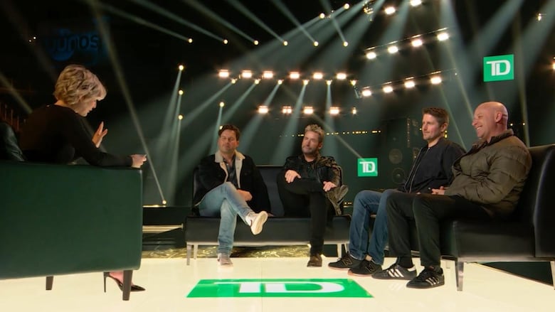 Five people are seated on a stage in square green chairs. Interview Kris Collins, a white woman with short blond hair, isn't facing the camera, and four white men, all members of Nickelback, face the camera.