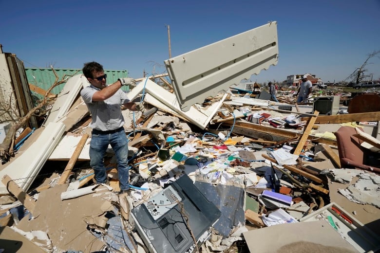 A man tosses objects onto a pile of tornado debris.