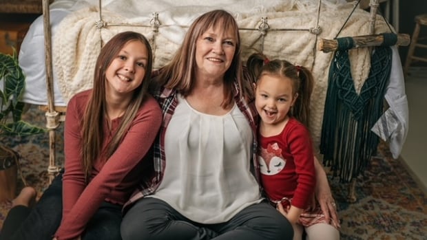 A woman sits between her two granddaughters in front of a bed.