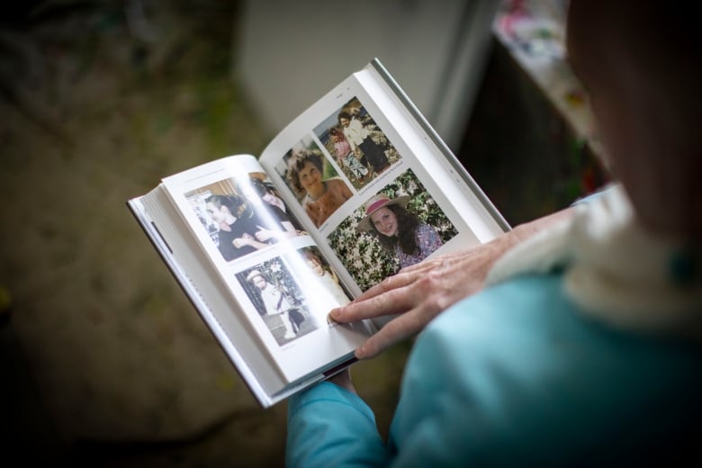 An open book is shown in the hands of a person wearing a robin's egg blue cardigan. The pages show several colour photographs of a girl throughout different stages of her life.