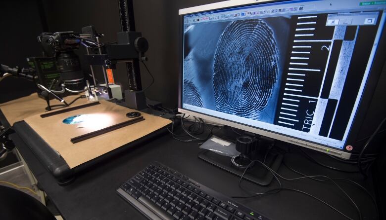 A computer monitor on a black desk in an ambiently lit room has a giant fingerprint blown up on it taking up the entire screen. 