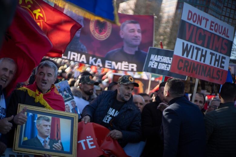 A crowd of protesters holding flags, signs and photos.