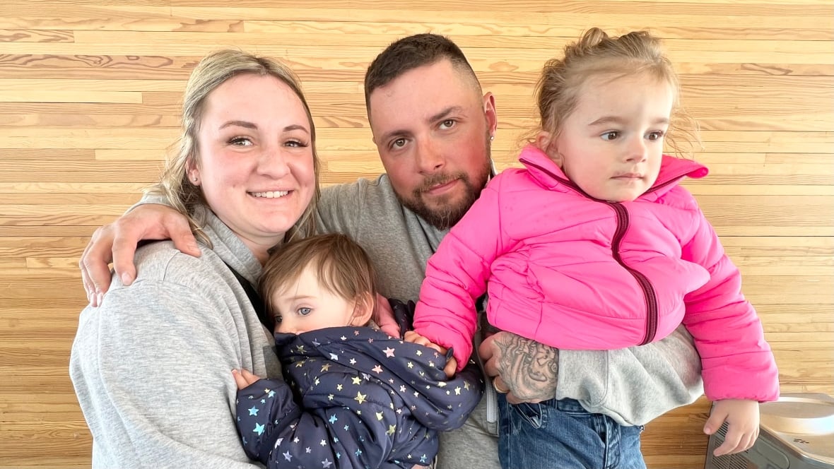 A family of four including two young girls hug.
