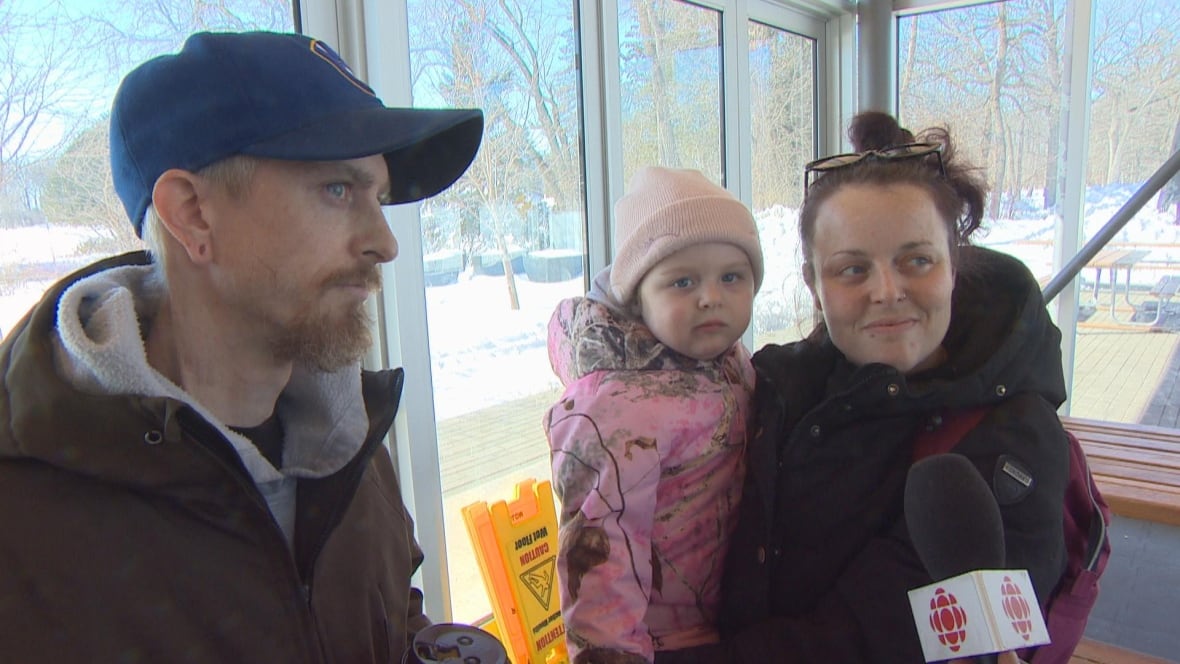 A couple hold their daughter in a warming hut in a park.
