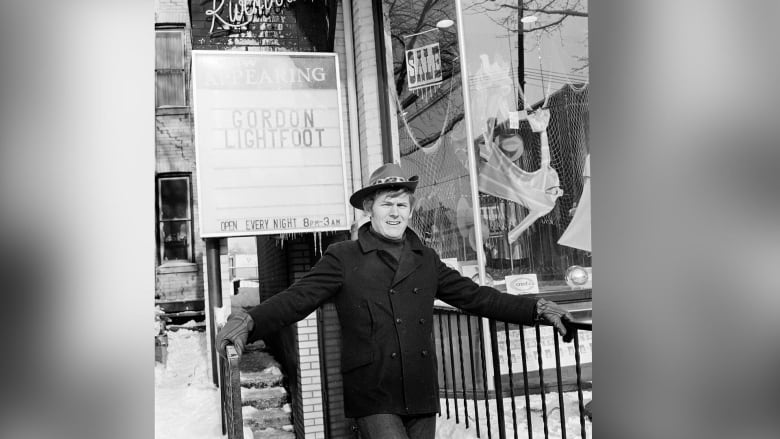 A man stands in front of a coffeehouse with a sign that says "now appearing" with his name: Gordon Lightfoot.