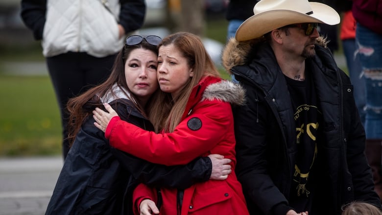 A woman in a bright red coat is pictured hugging another woman at the memorial service. 