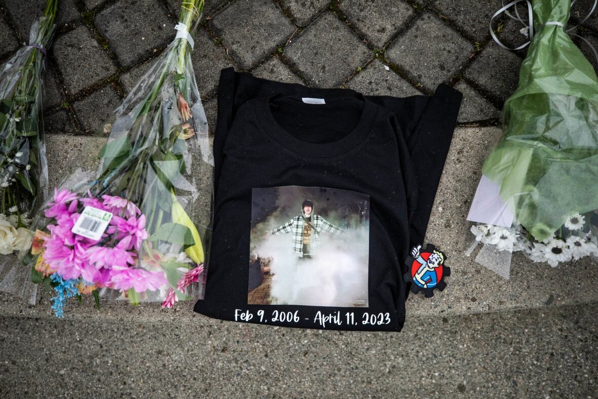 A black t-shirt with a photo of Ethan Bespflug on it is folded on the ground, next to bouquets of flowers. 