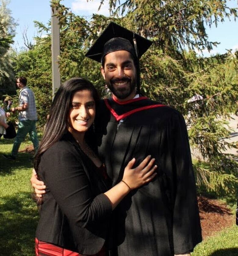 A smiling man in a black-and-red graduation robes with his arms around a smiling woman.   