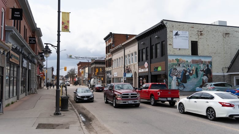 Cars driving down a downtown street surrounded by small shops.