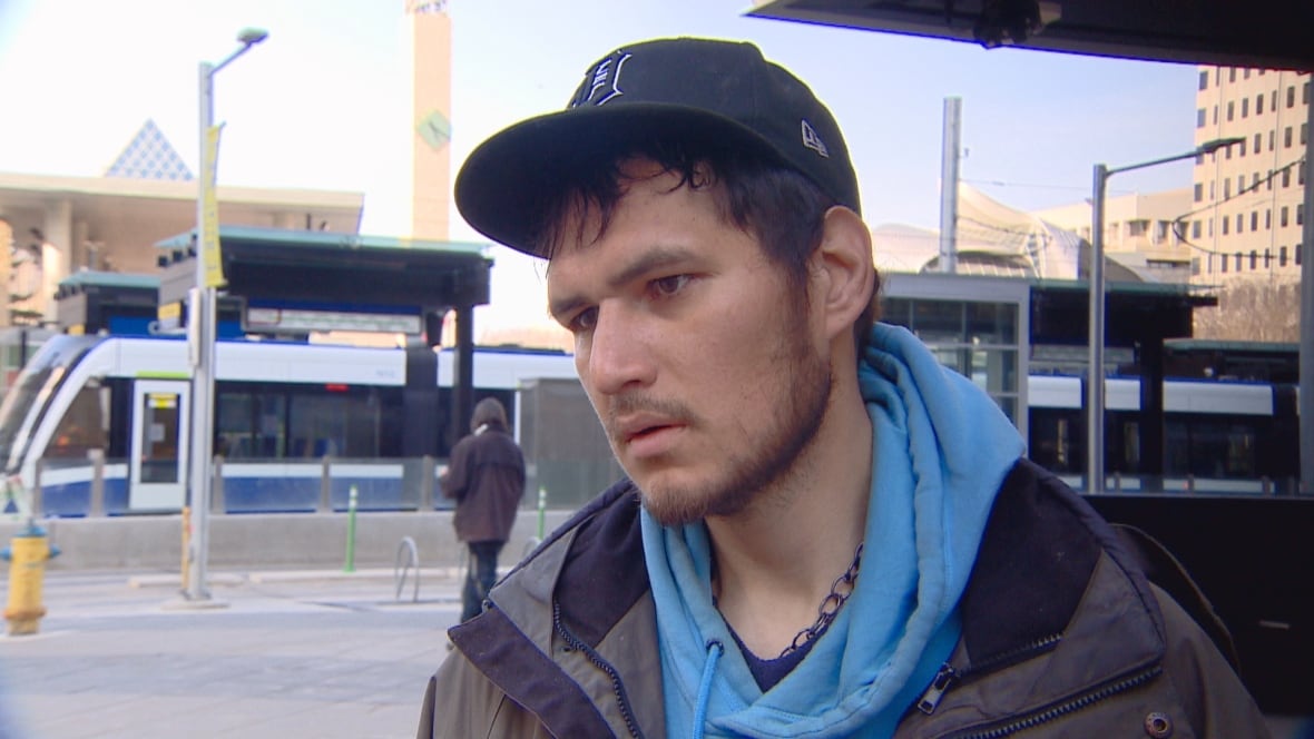 A man wearing a baseball cap stands on a city street, with an LRT train in the background.