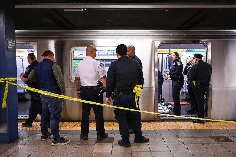 Police are seen outside a subway car that has been cordoned off by police tape.