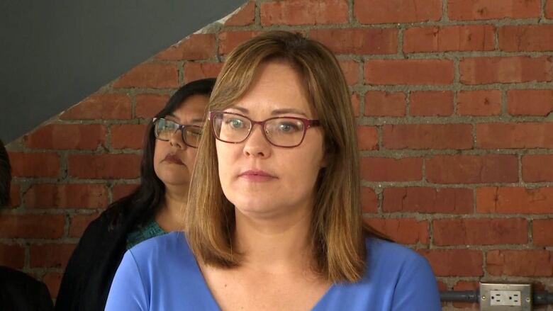 A woman stands in front of a brick wall.