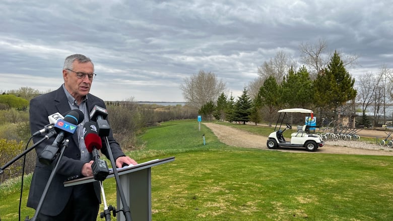A man can be seen standing at the podium with a golf cart in the background 