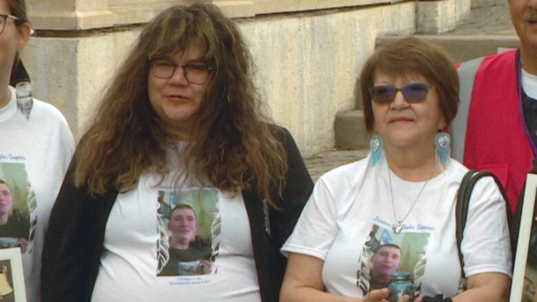 Two women wearing white T-shirts bearing the image of a young man.