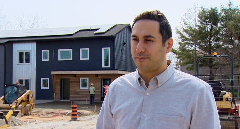 A man stands in front of a row of townhouses being built