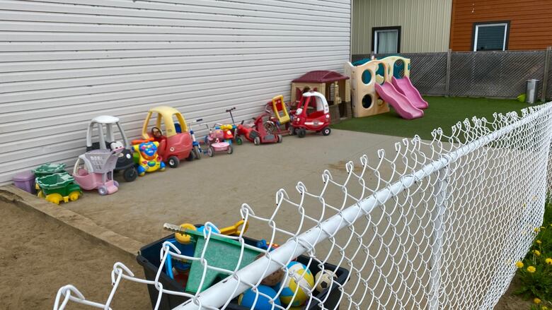 A daycare's outdoor playing space fenced in. Toys are seen beside a sandbox. 