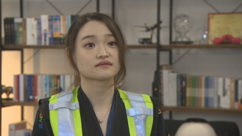 A woman wearing a safety vest stands in front of a book case.