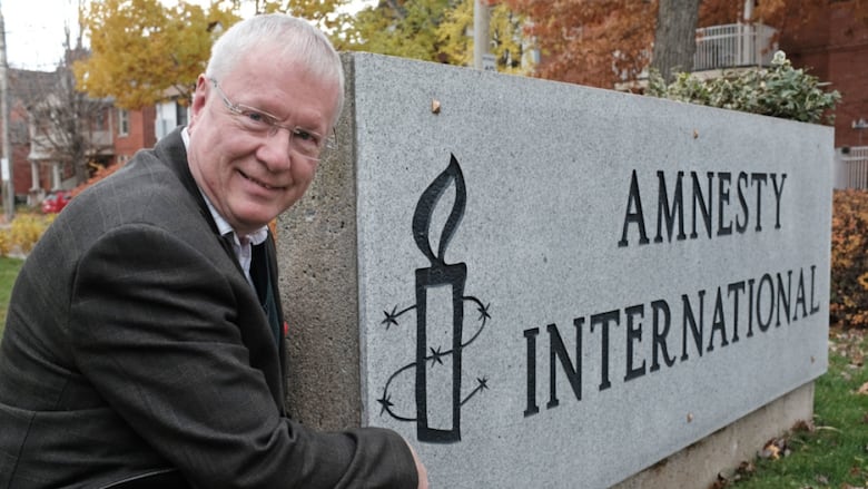 A man kneels next to an Amnesty International sign.
